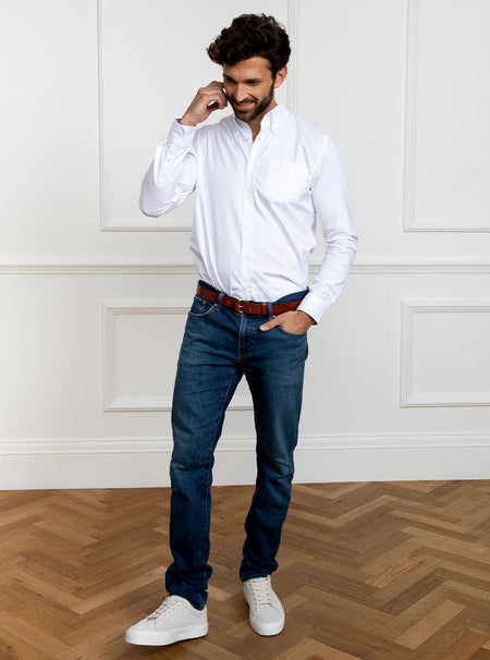 Man wearing white long sleeved shirt with button down collar and the inside collar and cuffs trimmed with sky blue. Made with 100% cotton in Thomas Mason fabric.